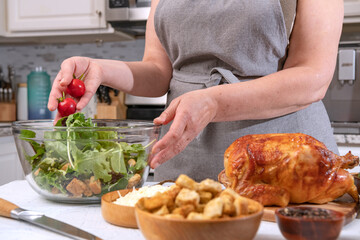 Cooking Caesar salad. Cook adds cherry tomatoes to glass bowl with salad in home kitchen.