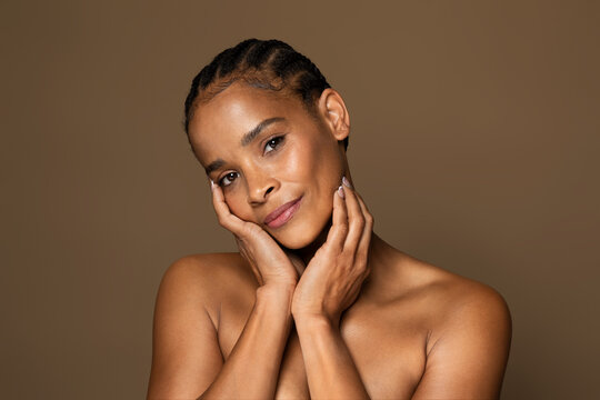 Antiage skincare concept. Beautiful black middle aged woman with flawless skin touching face and looking at camera