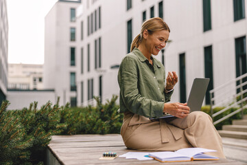 Smiling business woman via videoconference discuss project with colleague sitting on bench outdoors