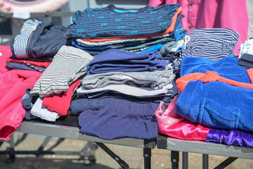 Used casual clothes in blue, white and pink for sale at a flea market stall on a sunny day