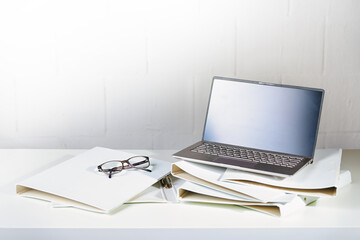 Laptop and glasses on several white ring binders on an office desk, administration and business...