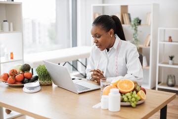 Friendly multiethnic female making video call via wireless device at doctor's workplace in...