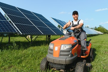 A man working at solar power station. A worker on a garden tractor mows grass on a solar panel farm.