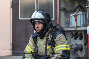 Obraz premium Portrait of a firefighter in a protective suit and a protective helmet sitting by a fire engine after working on a fire