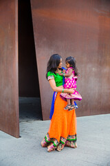 Fototapeta na wymiar beautiful indian family mom mother with daughter girl hugging and smiling with a bindi and traditional sari dress in front of a rust architectural building