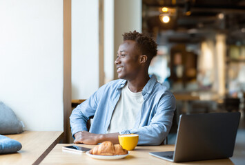 Smiling black guy using laptop computer at cozy cafe
