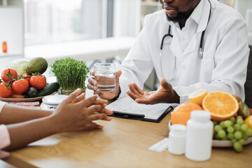 Cropped view of multiracial people discussing benefits of water while sitting at wooden desk in...