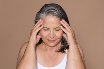 Sad senior caucasian woman with gray hair touches head, suffering from migraine