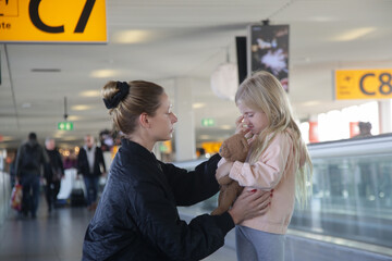 Young woman comforting child lost at the airport who can't find her parents. Mother consoling upset little crying girl which got scared from flight at the airport.