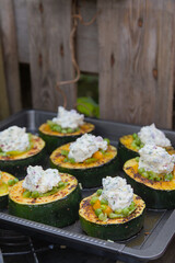 Zucchini slices stuffed with peas and carrots topped with cream cheese on a baking sheet.