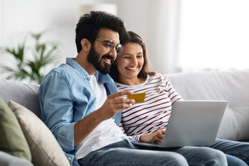 Happy indian couple with bank card and laptop at home