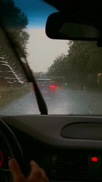 Car driving through a heavy rain on a highway. Raindrops seen through the interior of a vehicle while a man drives, vertical video background.