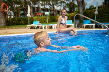 Naklejka premium Young boy kid child eight years old splashing in swimming pool having fun leisure activity. Boy happy swimming in a pool. Activities on the pool, children swimming and playing in water, happiness and