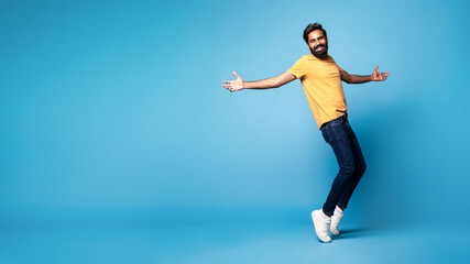 Fototapeta premium Joyful middle aged indian man in casual standing on toes and smiling at camera, panorama with free space