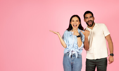 Naklejka premium Cute loving multiracial couple pointing at free space on pink