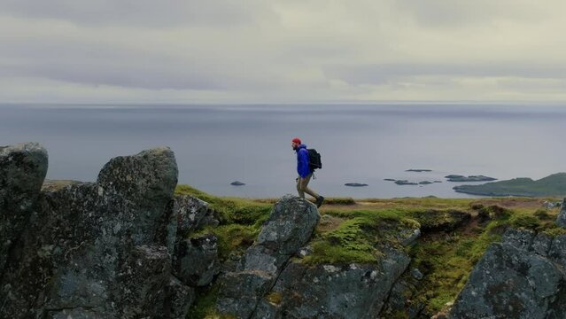 Young male traveler hikes alone at the top of the fjord and observes stunning views of Lofoten islands