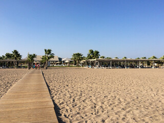 View of the wooden path in perspective from the sea beach to the hotel buildings. Tourists walk...