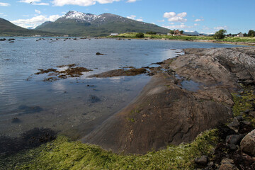 Seashore with clear water and protruding rocks overlooking snow-capped mountains in summer