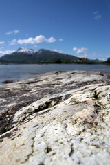 Textured gray rock on the seashore with a view of the mountains and the sea on a sunny day