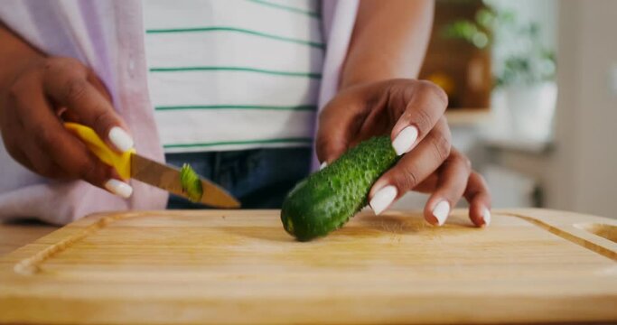 Women's hands are cutting a cucumber while preparing a salad in the kitchen, there is no face