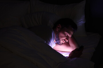 Fototapeta na wymiar Man using smartphone in bed at night. Internet addiction
