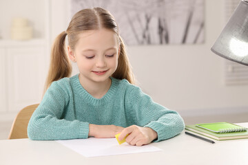 Girl using eraser at white desk in room