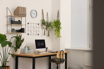 Cozy workplace with computer, modern furniture and houseplants at home