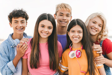 Group of smiling friends, multiracial teenagers wearing colorful t shirts hugging standing outdoors. Happy stylish boys and girls on street looking at camera. Friendship, positive lifestyle, summer