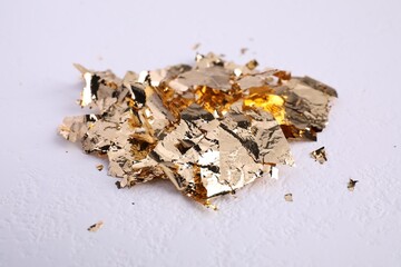 Many pieces of edible gold leaf on white textured table, closeup