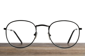 Stylish glasses with metal frame on wooden table against white background