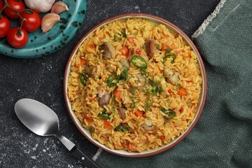 Delicious pilaf with meat and ingredients on black textured table, flat lay