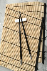 Bamboo mat with pair of black chopsticks and rest on table, top view