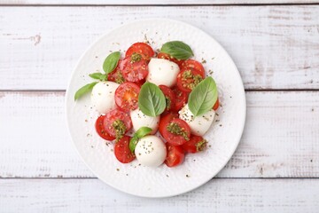Tasty salad Caprese with tomatoes, mozzarella balls and basil on white wooden table, top view