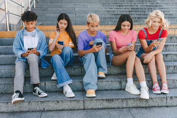 Group of serious friends, multiracial teenagers holding mobile phones watching video, chatting,...