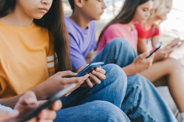 Group of serious multiracial teenagers holding mobile phones watching video, communication online, chatting, selective focus. Technology, social media concept