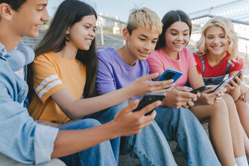 Group of smiling friends, multiracial teenagers holding mobile phones watching video, communication online, playing mobile game, talking sitting on stairs. Technology, social media concept