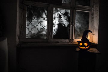 Scary Halloween pumpkin in the mystical house window at night or halloween pumpkin in night on room with blue window. Symbol of halloween in window. Selective focus