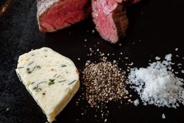 Top view and selective focus at beef steak serve with butter, slaz and black pepper, on the black plate and wooden table. 