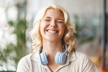 Authentic portrait of smiling cute school girl with eyes closed wearing wireless headphones....