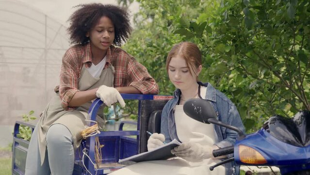 Happy children girl farmer sitting on tricycle in hydroponics farm talking together with worker to take notes on clipboard, Biotechnology kid with Skylab motorcycle transportation at vegetable farm