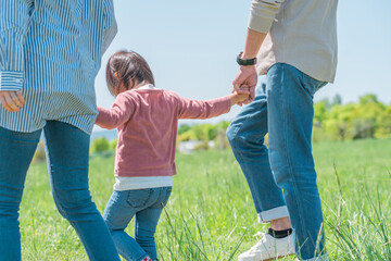 空の見える公園で手を繋いで歩く子供と両親のアジア人家族・ファミリーの後ろ姿
