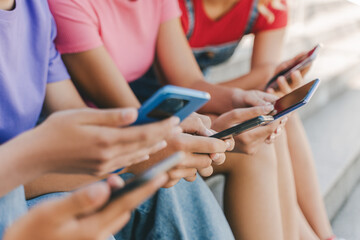 Closeup, group of teenagers holding mobile phones watching video, communication online, chatting, selective focus. Technology, social media concept  