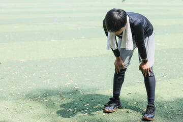 Tired young  runner man with towel round his neck taking a rest after running hard at the park
