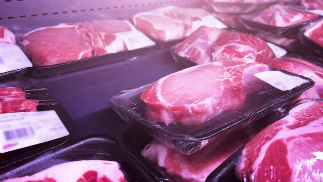 Raw fillets of pork, beef or turkey steaks in plastic containers covered with cling-wrap in a supermarket refrigerator. Close-up shot