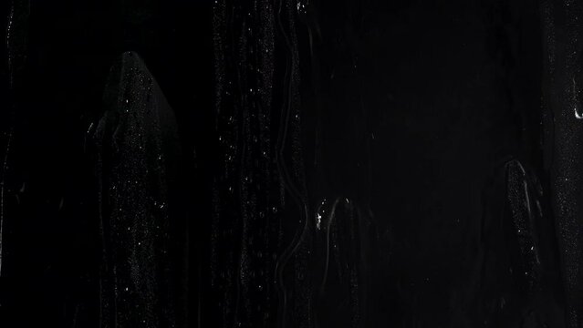 Water washing away droplets on a windowwater on glass window on a black background