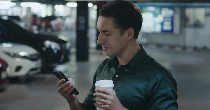 stylish guy in green shirt using smartphone chatting social media addict. man typing messages drinking coffee while standing parking of lights background concept social media addict