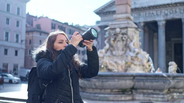 Happy young Latin woman tourist in warm clothes looking away with professional photo camera while standing in front of the Pantheon in Rome, Italy