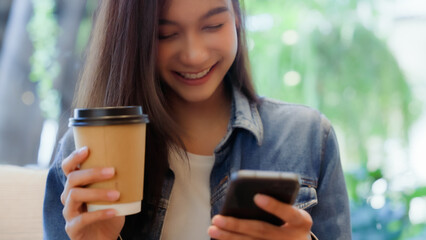 Asian woman happy and typing messages on smartphone in cafe Smiling young woman sitting at table with hot cup of coffee and using mobile phone