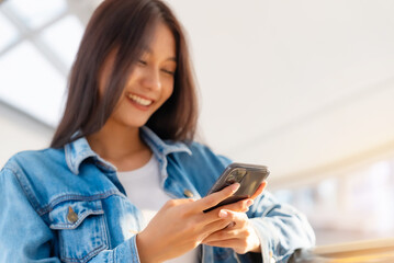 Fototapeta na wymiar Close up hand of young asian woman smiling using mobile smart phone outdoor. Happy female tourist wearing jeans jacket and holding smartphone at public