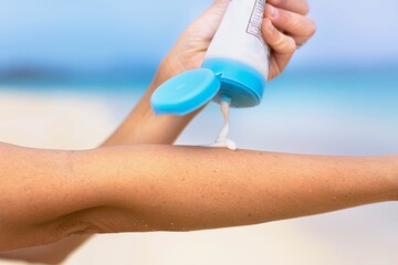 A woman applying sunblock on her skin outdoor on a sunny day at the beach.